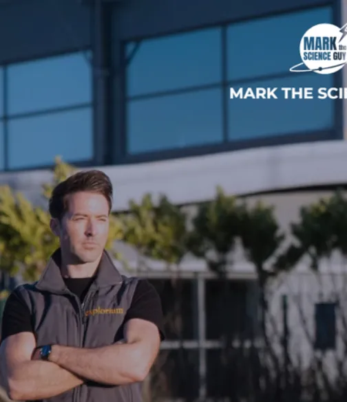 Mark the Science Guy stands with his arms crossed outside a modern building, with the “Mark the Science Guy” logo displayed in the upper-right corner.