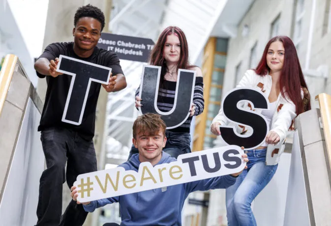 Four young adults are posing on a staircase, holding up letters that spell 